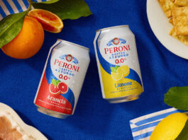 Peroni 0.0% expands alcohol free range with flavoured offer Cans of Peroni 0.0% Arancia Rossa and Limone di Sicilia sit at the middle of a table with a blue tablecloth on top with lemons and blood oranges around the cans and food.