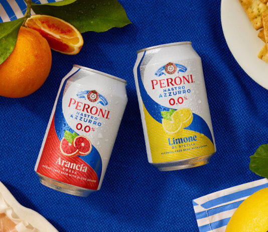 Peroni 0.0% expands alcohol free range with flavoured offer Cans of Peroni 0.0% Arancia Rossa and Limone di Sicilia sit at the middle of a table with a blue tablecloth on top with lemons and blood oranges around the cans and food.