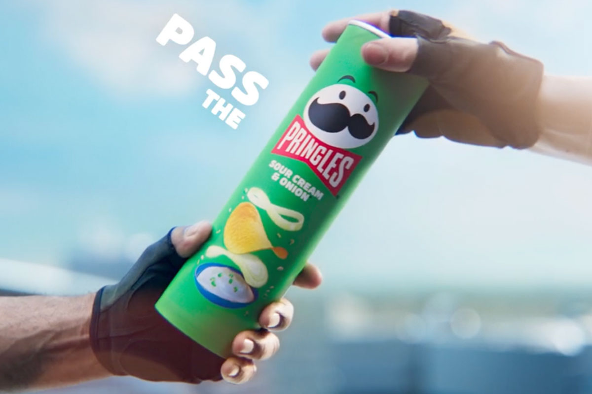 A person passes a tube of Pringles Sour Cream & Onion to another person.
