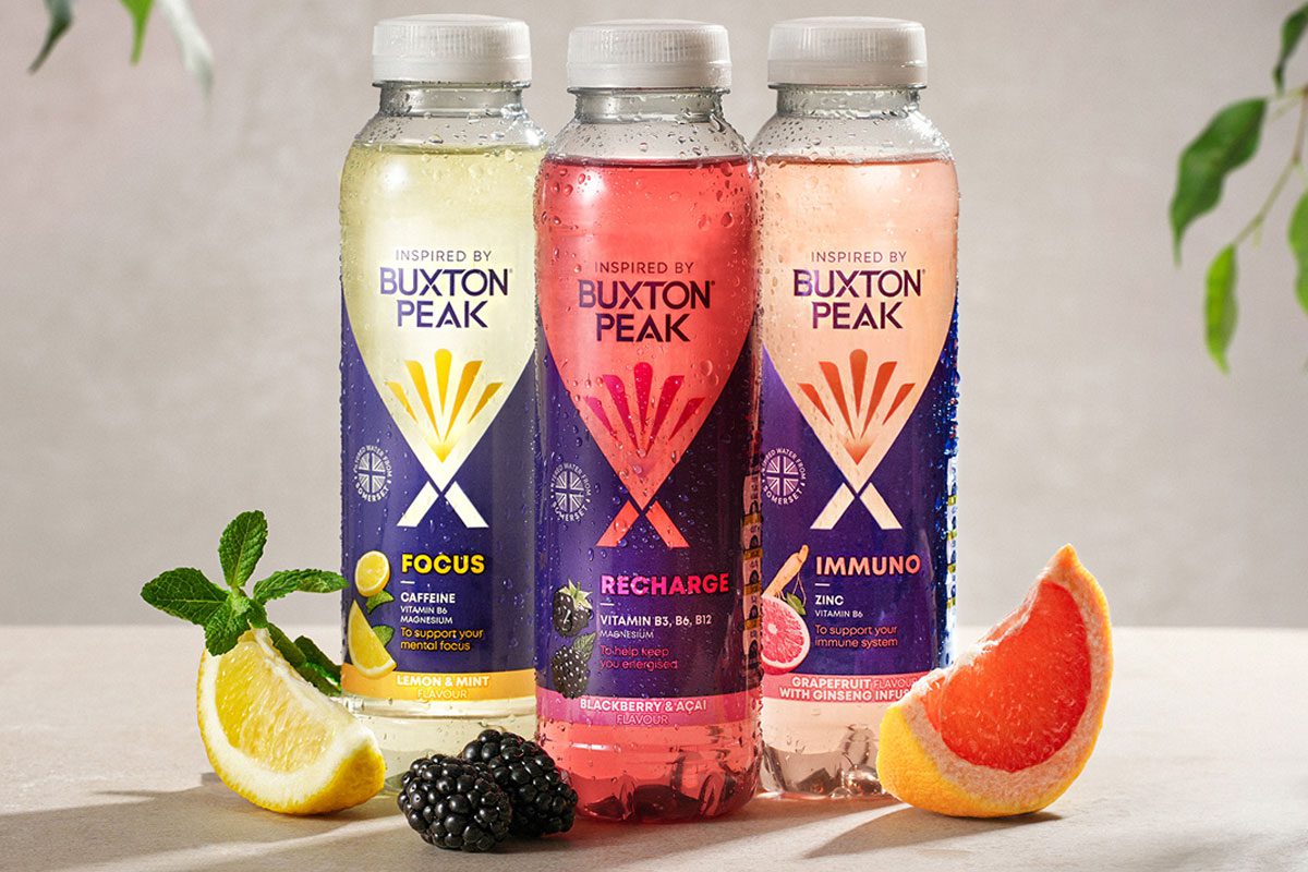 Bottles of Inspired by Buxton Focus, Recharge and Immuno stand together with pieces of fruit around the three.