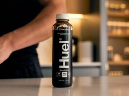 Danone set to acquire Huel meal solutions A bottle of Huel Chocolate Black Edition sits on a countertop with a person behind the bottle.