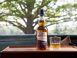 Glen Moray beckons temptation with Forbidden Fruit launch A bottle of Glen Moray Forbidden Fruit stands on a wooden tray with a rocks glass beside it. In the background is a tree.