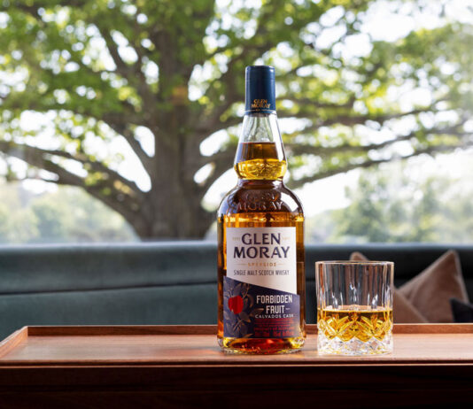 Glen Moray beckons temptation with Forbidden Fruit launch A bottle of Glen Moray Forbidden Fruit stands on a wooden tray with a rocks glass beside it. In the background is a tree.