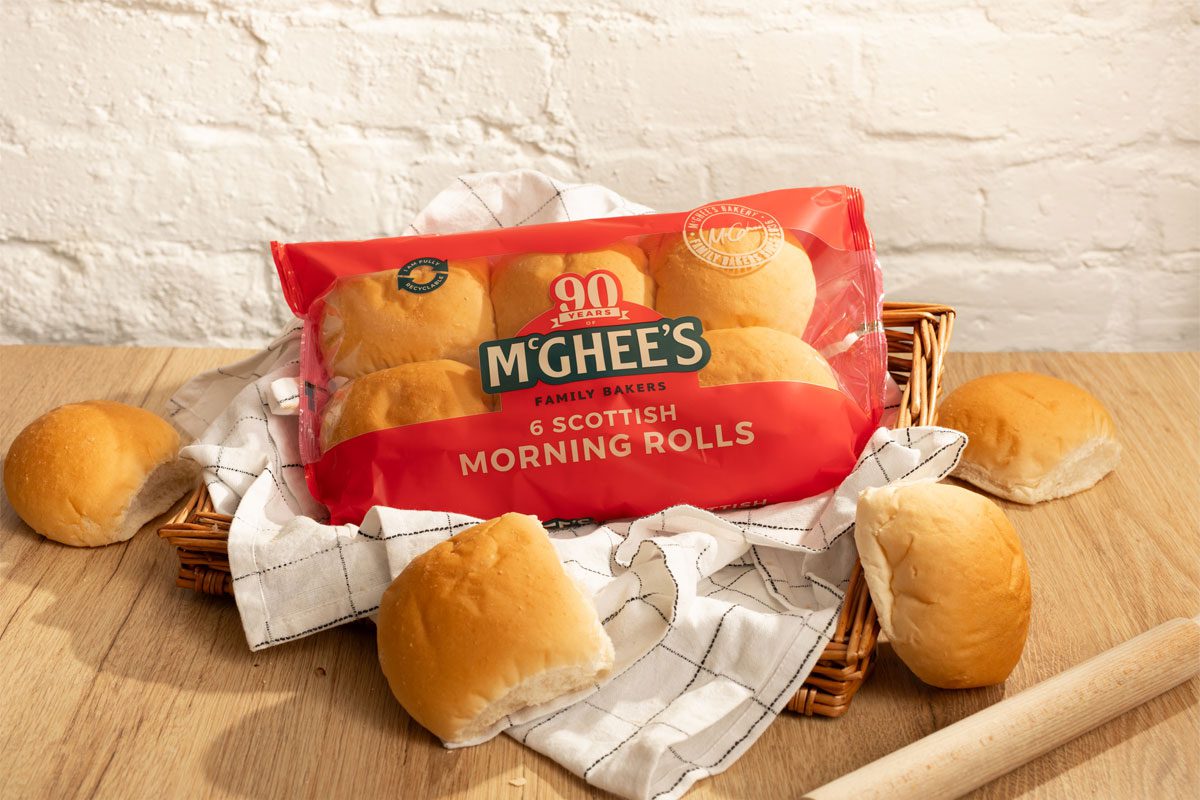 A packet of McGhee's Morning Rolls sit in a bread basket with a tea towel with individual rolls around the basket.