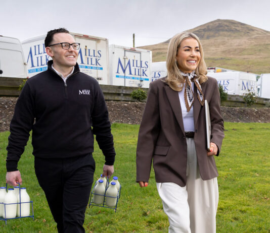 Mills Milk targets further expansion after £24m turnover result Members of the Mills Milk team stand in a field with branded vans behind them and a hill in the distance.