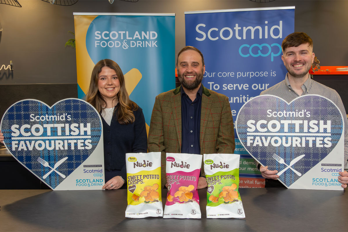 Lauren Rafferty, commercial development coordinator at Scotmid, Rodney Garnham, managing director at Nudie Snacks and Steve Addison, local sourcing manager at Scotmid, all stand at a table for the Scottish Favourites competition with packs of Nudie Snacks sweet potato crisps.