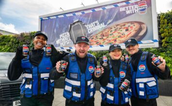 Pepsi Max launches multi-channel campaign A group of people stand in front of a billboard featuring the 2026 Pepsi Max campaign whilst holding cans of Pepsi Max.