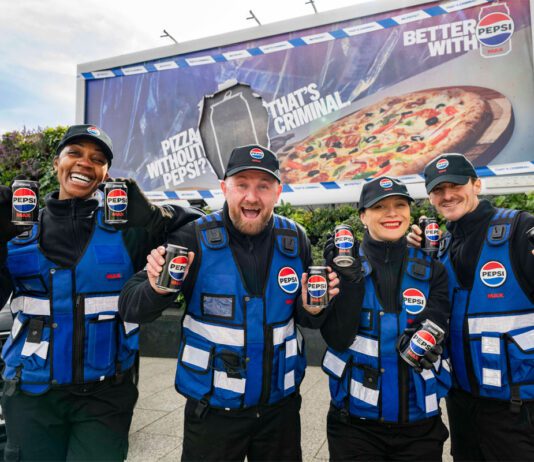 Pepsi Max launches multi-channel campaign A group of people stand in front of a billboard featuring the 2026 Pepsi Max campaign whilst holding cans of Pepsi Max.