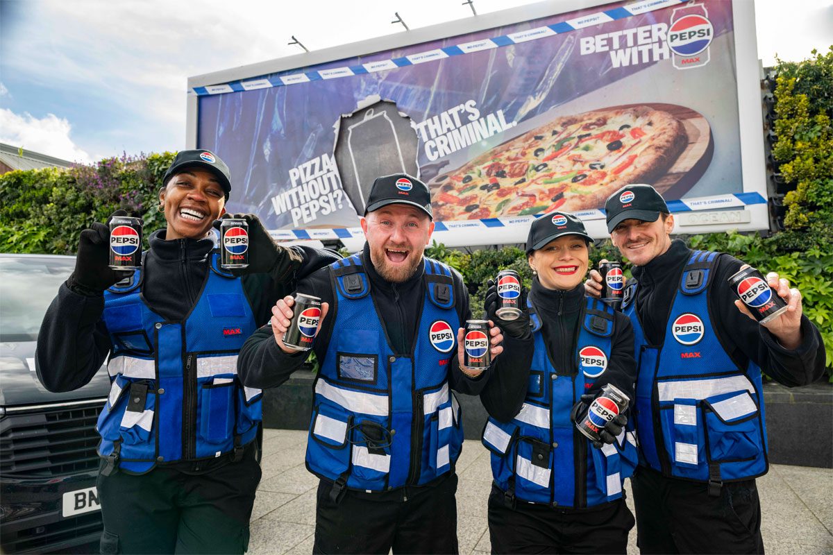 A group of people stand in front of a billboard featuring the 2026 Pepsi Max campaign whilst holding cans of Pepsi Max.