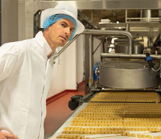 Andy Murray makes a visit to Walker’s Shortbread factory Andy Murray stands over a conveyer belt with shortbread on it.
