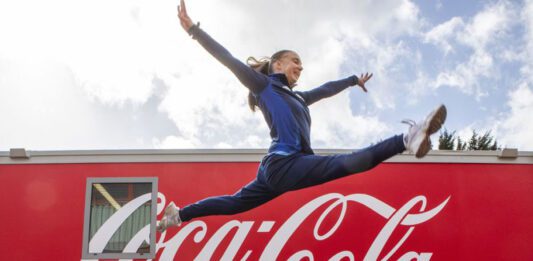 Coca-Cola announced as Soft Drinks Partner of Glasgow Commonwealth Games A woman jumps over the Coca-Cola logo.