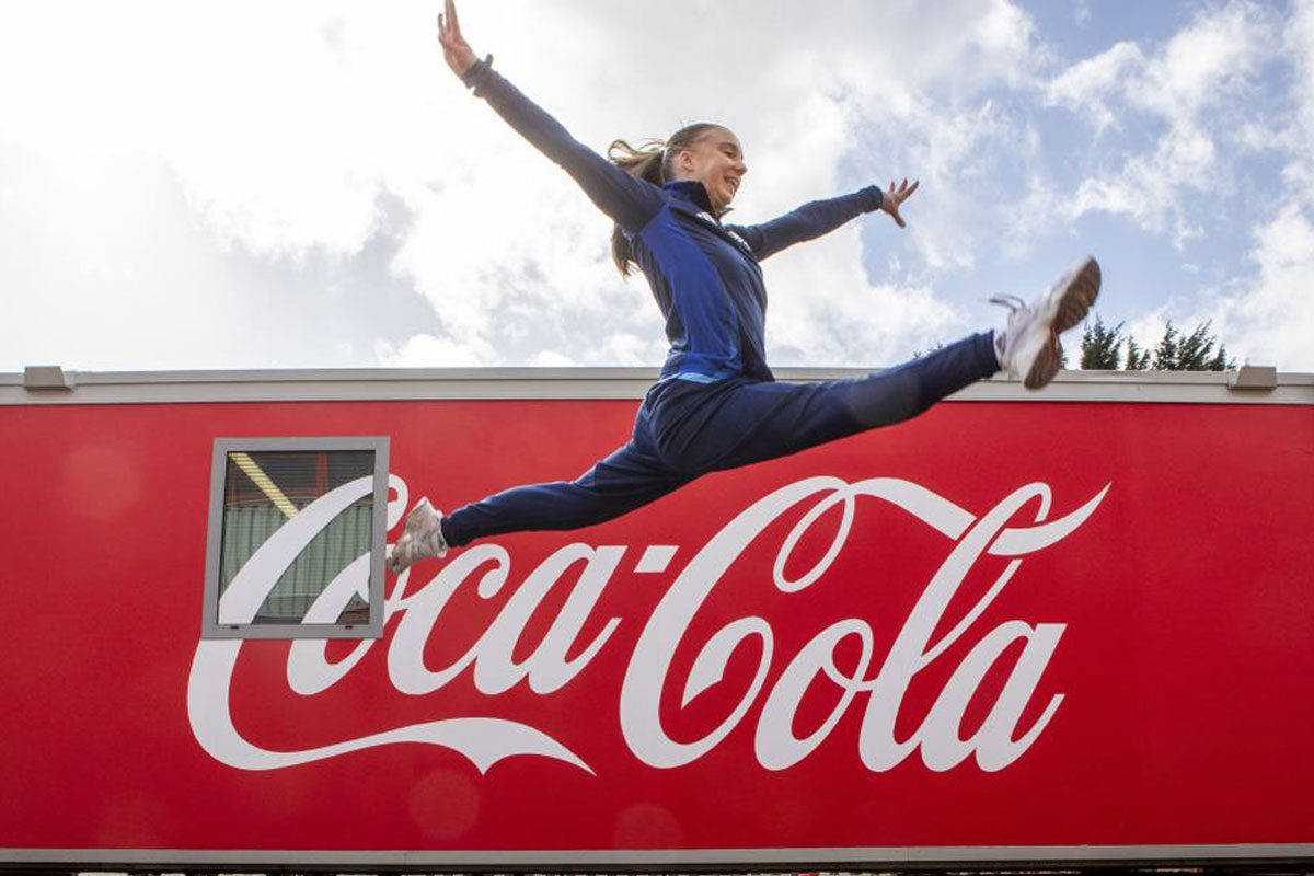 A woman jumps over the Coca-Cola logo.