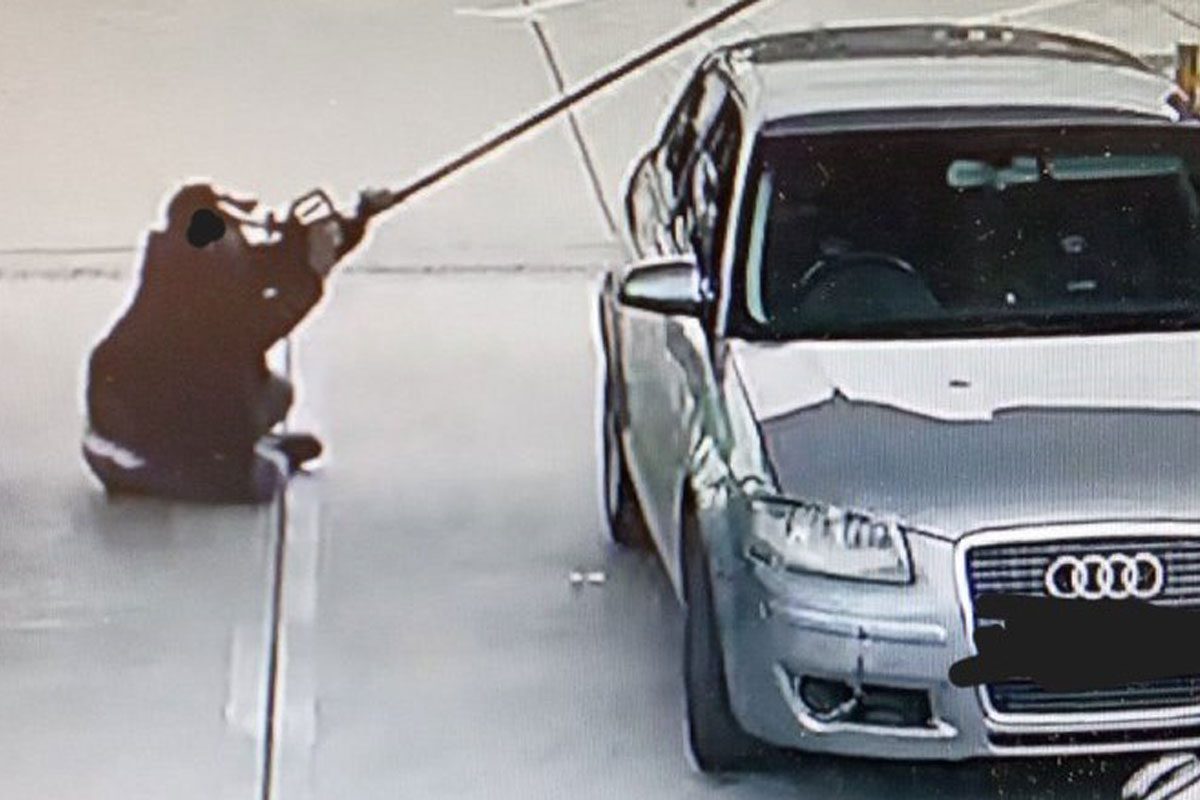 A person sits in a forecourt fuel station holding a fuel nozzle up close to their face.