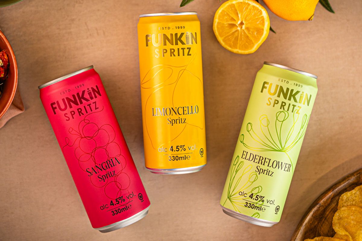 Cans of Funkin Spritz are laid out across a table with sliced oranges above them and a bowl of crisps to the bottom right and olive to the top left.