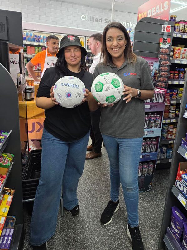 Nathalie Fullerton, owner of Go Local Dumbarton Road, stands with a person, the pair are holding signed footballs.