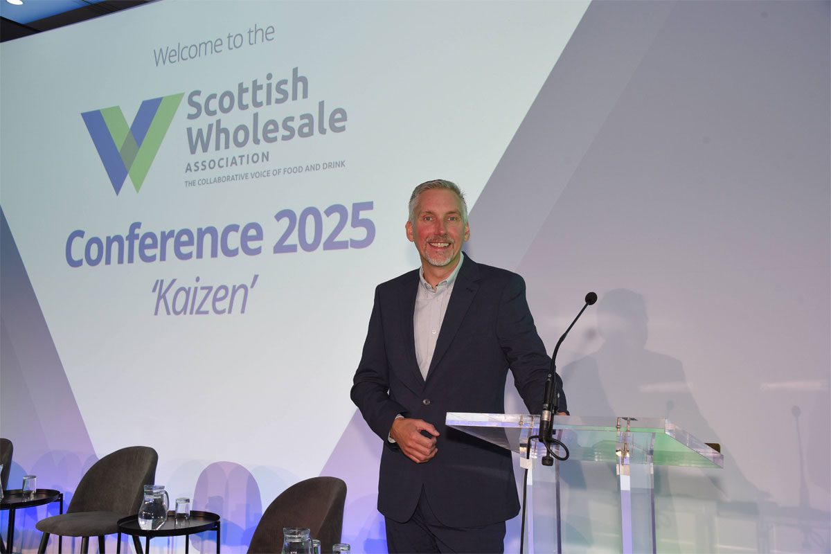 Colin Smith, chief executive at the Scottish Wholesale Association, stands at a lectern on a stage at the SWA 2025 Annual Conference.
