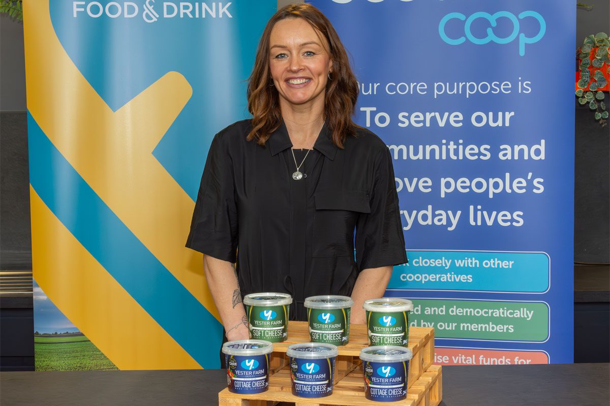 A woman stands behind a table with pots of Yester Farm Dairies Cottage Cheese on it.