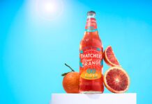 Thatchers introduces new Blood Orange 0.0% cider A bottle of Thatchers Blood Orange 0.0% stands on a white podium with blood oranges around it with a sunny background.