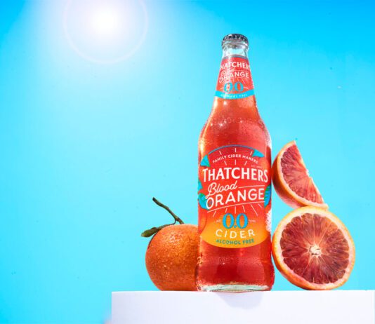 Thatchers introduces new Blood Orange 0.0% cider A bottle of Thatchers Blood Orange 0.0% stands on a white podium with blood oranges around it with a sunny background.