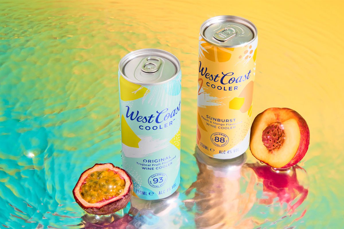 Cans of West Coast Cooler Original and West Coast Cooler Sunburst stand on a watery surface with a passionfruit and peach standing next to them.