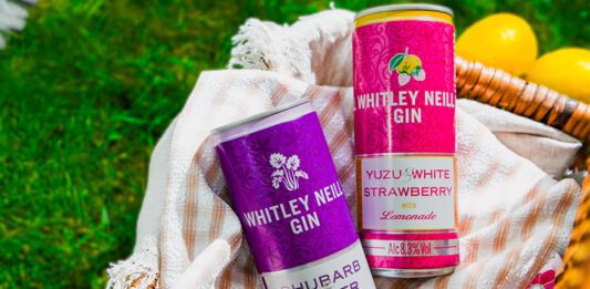Whitley Neill enters into RTD market Cans of Whitley Neill Rhubarb & Ginger with Ginger Ale and Yuzu & White Strawberry with Lemonade sit in a wicker basket on grass with lemons around the basket.