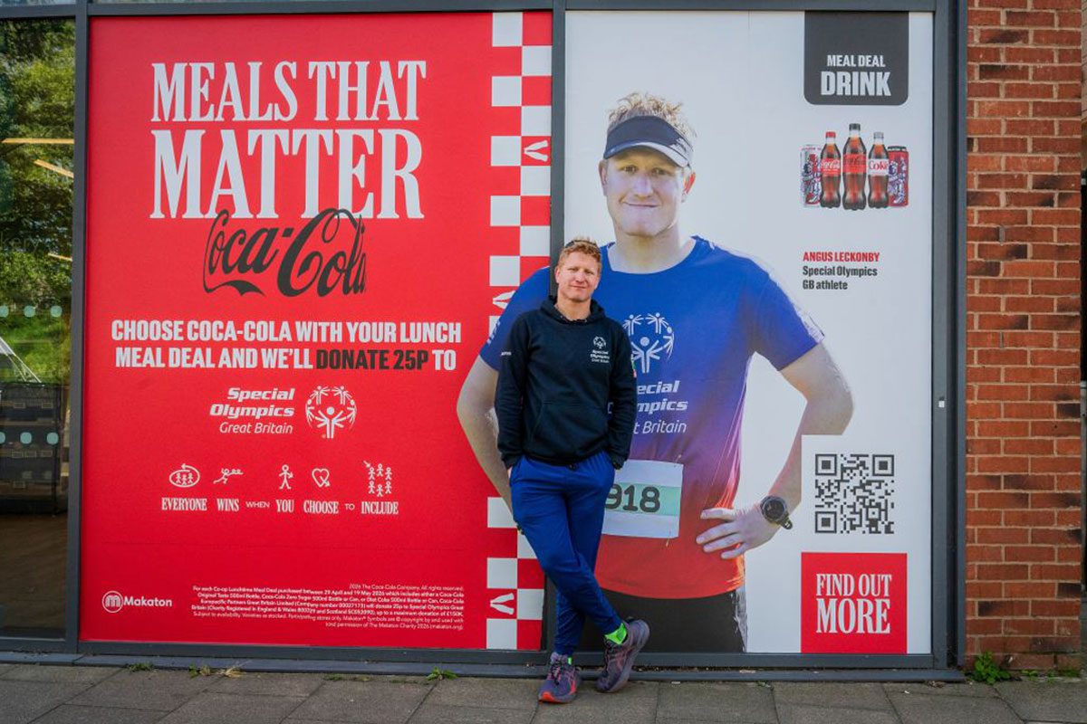 Angus Leckonby, Special Olympics GB Athlete, stands in front of the CCEP Meals that Matter promotional image which features him.