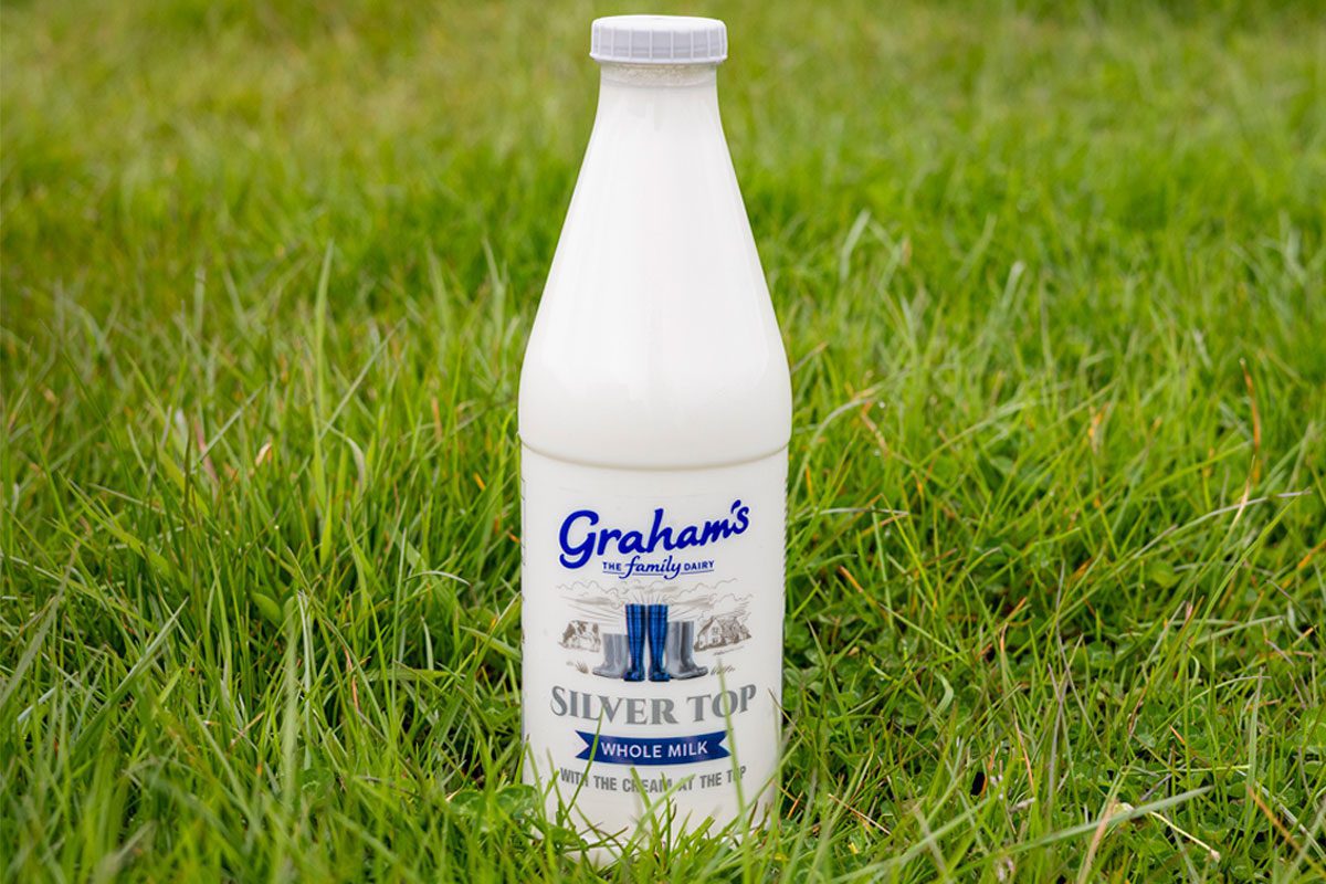 A bottle of Graham's Silver Top milk stands in a grassy field.