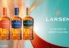 Larsen Cognac unveils new premium bottle design Promotional image of the Larsen Cognac redesign for 2026 featuring the new bottles next to the company logo with text that reads "A Century of Smooth Sailing".
