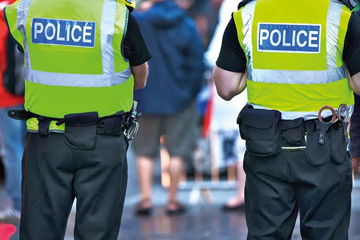Two police officers stand with their backs to the camera in the middle of a busy street.