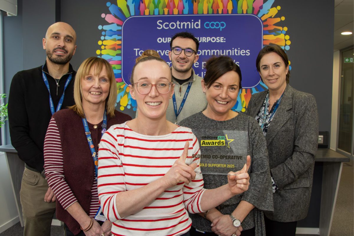 Members of the Scotmid team stand together in their office holding the GroceryAid Gold trophy.