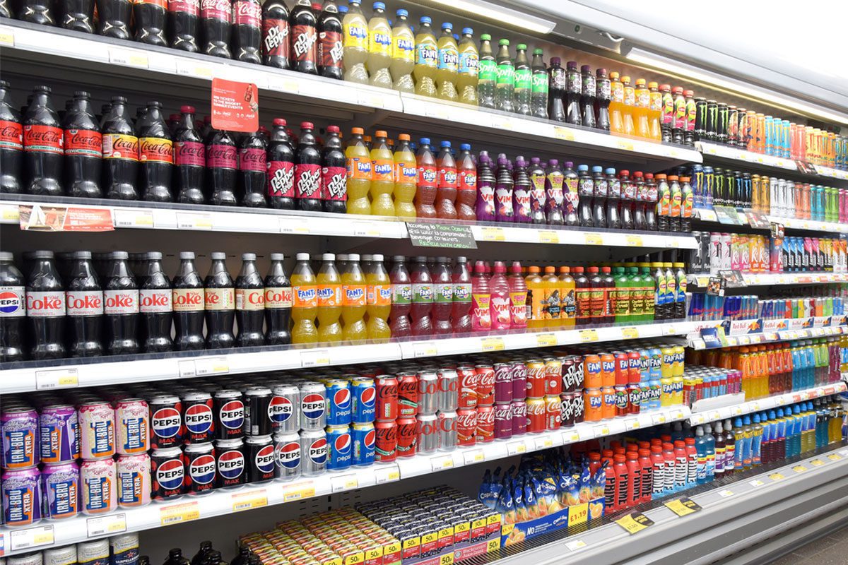 A refrigerator unit inside a retail store with soft drinks in it.