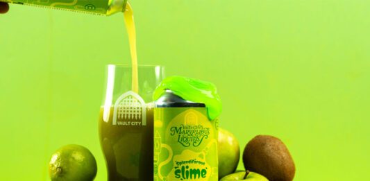 Vault City dials up sour tastes with Marvellous Liquids range A can of Vault City Splendiferous Slime stands amongst green fruit with green slime on top of the can whilst the beer is poured out into a Vault City glass behind the can.