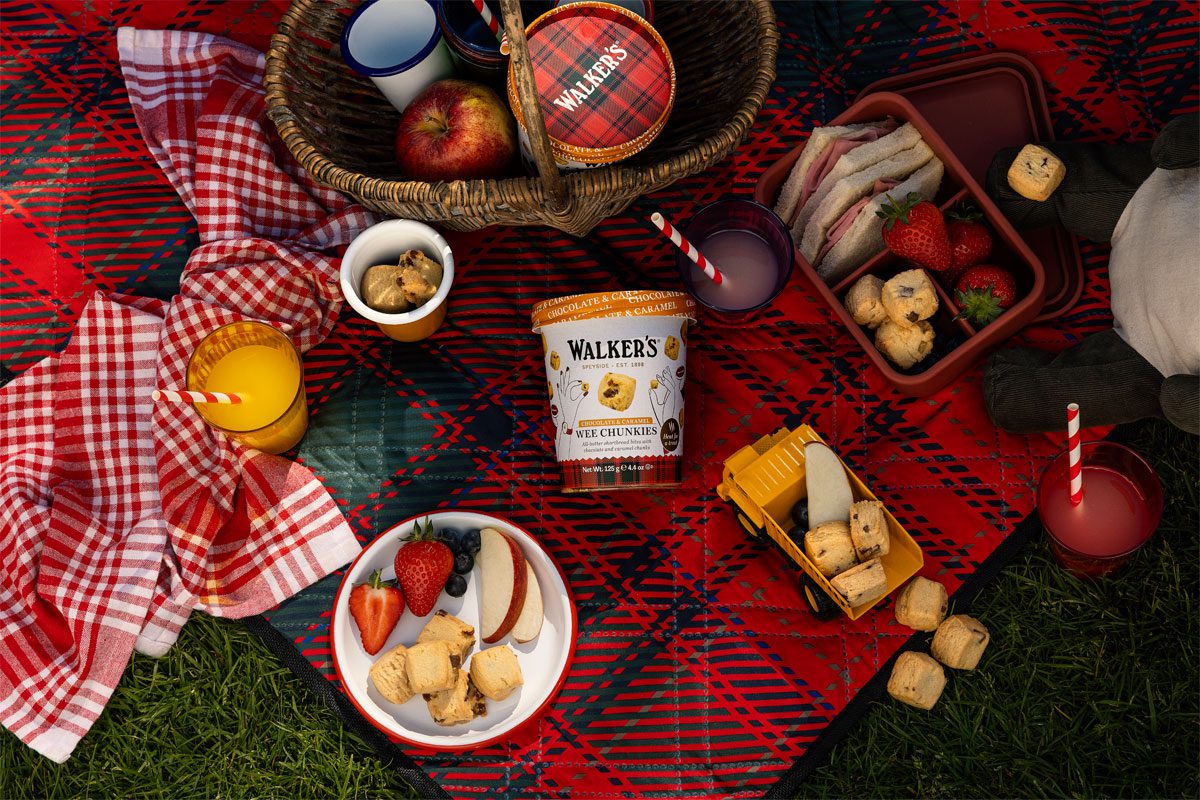 A picnic scene featuring the new Walker's Shortbread Wee Chunkies Chocolate & Salted Caramel Tub.