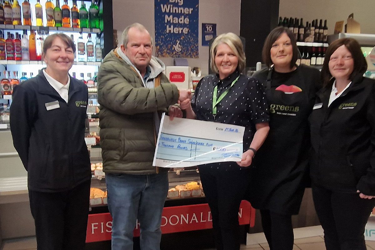 A group of people stand in Greens of Fraserburgh to present a cheque to a local charity group.