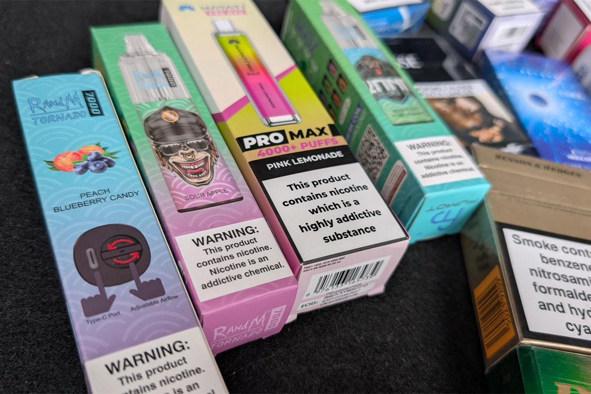 Packs of illicit disposable vapes sit on a counter.