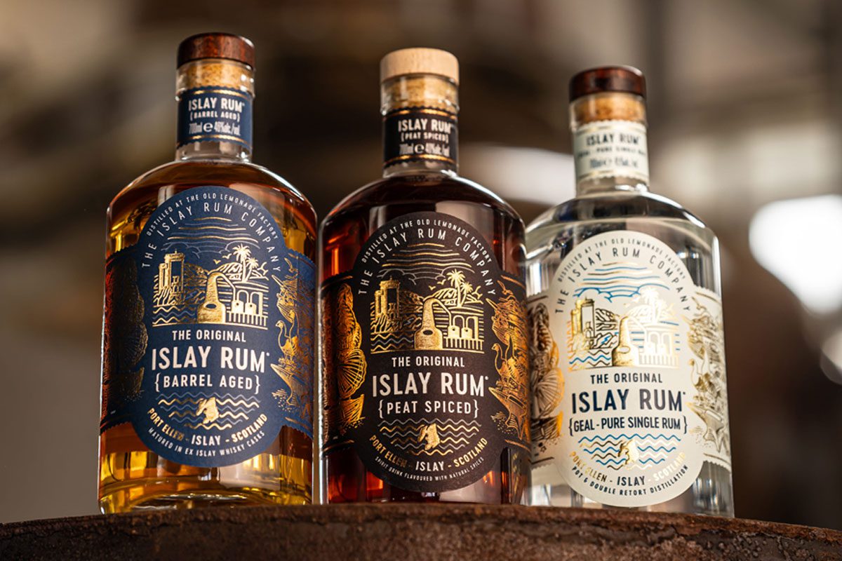 Bottles of The Original Islay Rum Barrel Aged, The Original Islay Rum Geal and The Original Islay Rum Peat Spiced sit on top of a barrel inside the distillery.