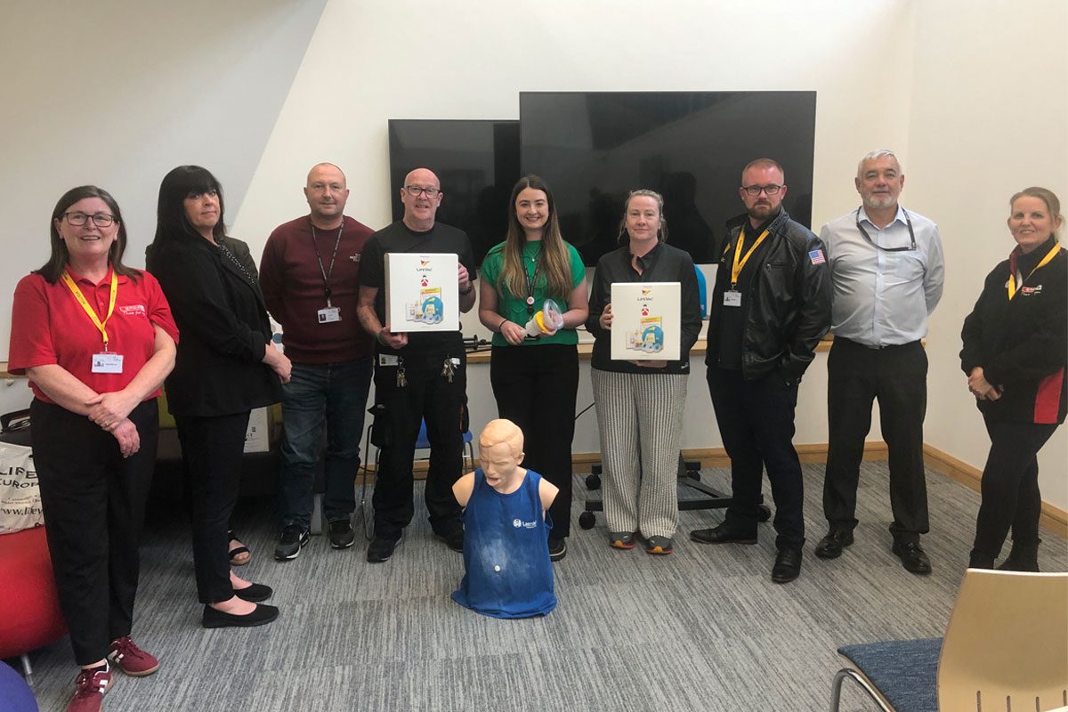 A group of people stand together in a classroom setting with LifeVac devices as well as a practice dummy on the floor.