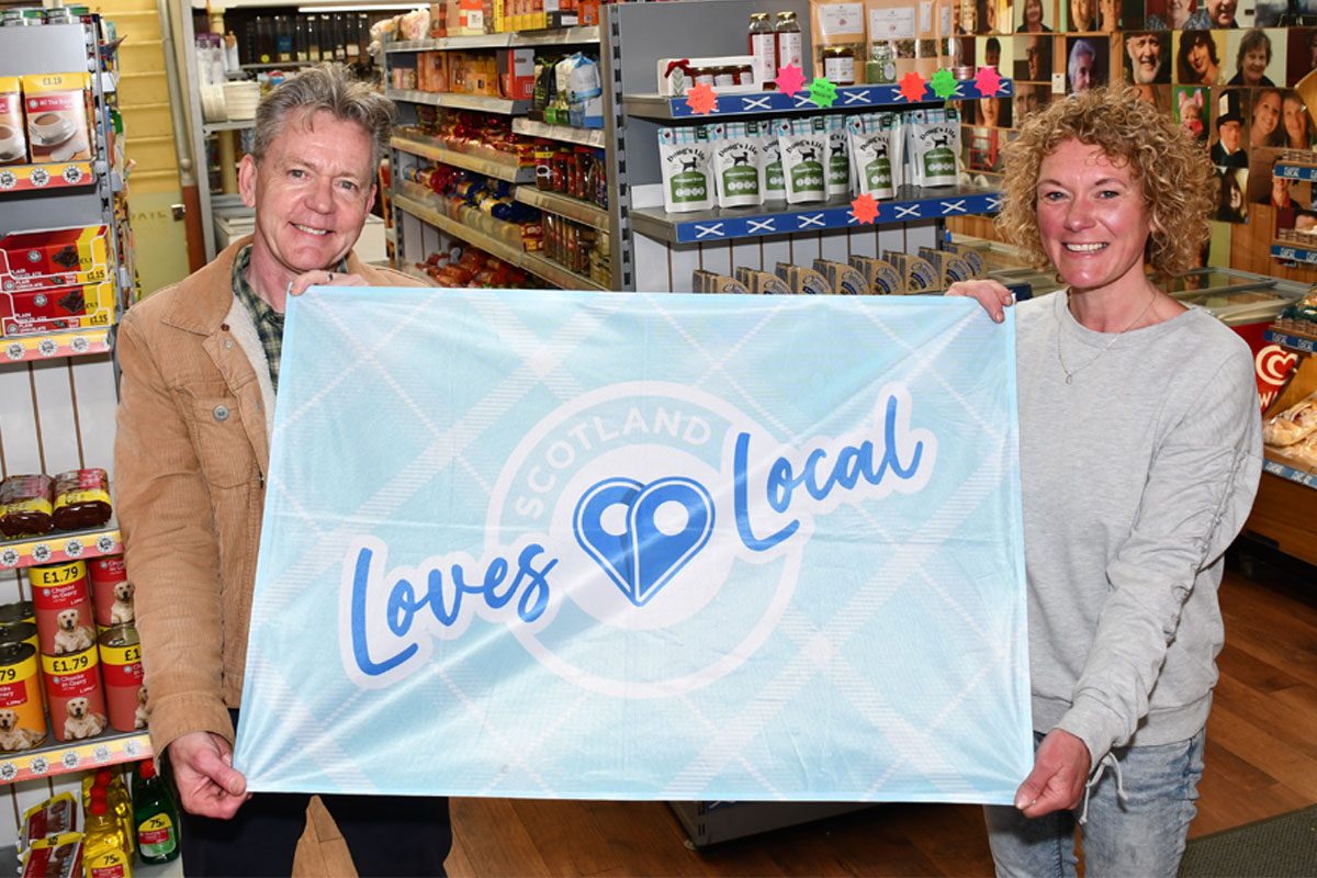 Graham Watson, president at the SGF, stands holding a flag with the Scotland Loves Local logo on it with colleague Katie McKenzie-Wilson.