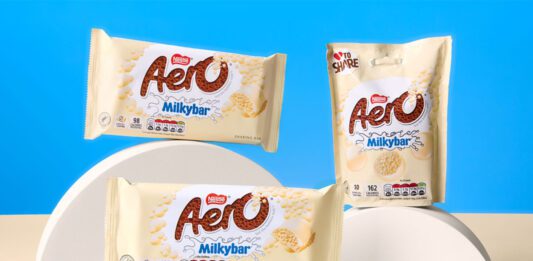 Nestlé unveils new Aero Milkybar range Packs of Aero Milkybar and Aero Milkybar Buttons are stacked on semi-circle shapes against a blue background with a white table.