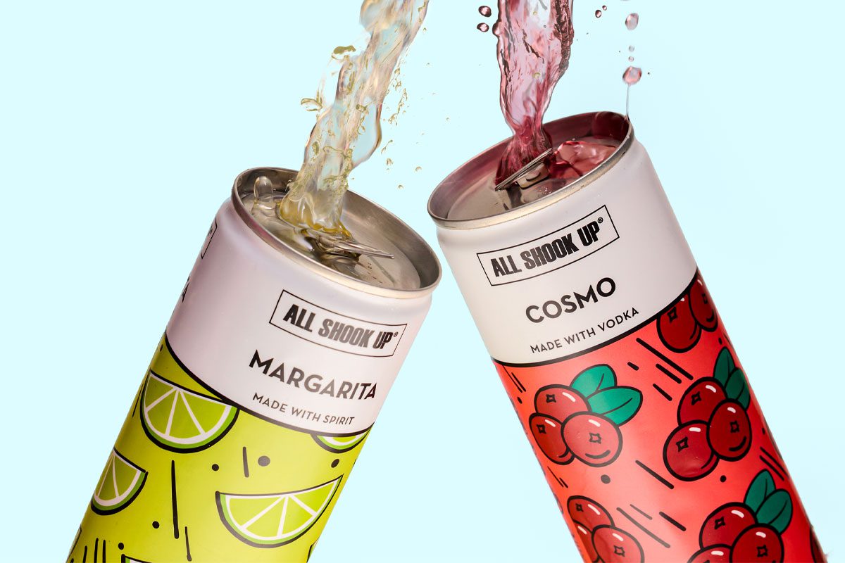 Cans of All Shook Up Margarita and Cosmo are clinked together as the cocktails spill out the top of the cans against a blue background.