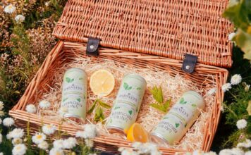 Darnley’s Gin enters the RTD market with Elderflower Spritz Cans of Darnley's Elderflower Gin Spritz lie in a basket with pieces of mint and lemon around them. The basket sits on a grassy field with flowers.