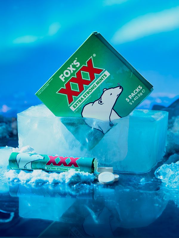 A multipack of Fox's XXX Mints is frozen in a block of ice with a single pack in front of this with some of the mints spilling out from the pack.