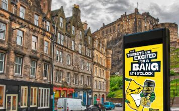 Hooch unveils “no-nonsense” multi-media campaign An image of a street in Edinburgh with Edinburgh Castle in the skyline. The Hooch summer 2026 campaign is on the digital screen in the foreground.