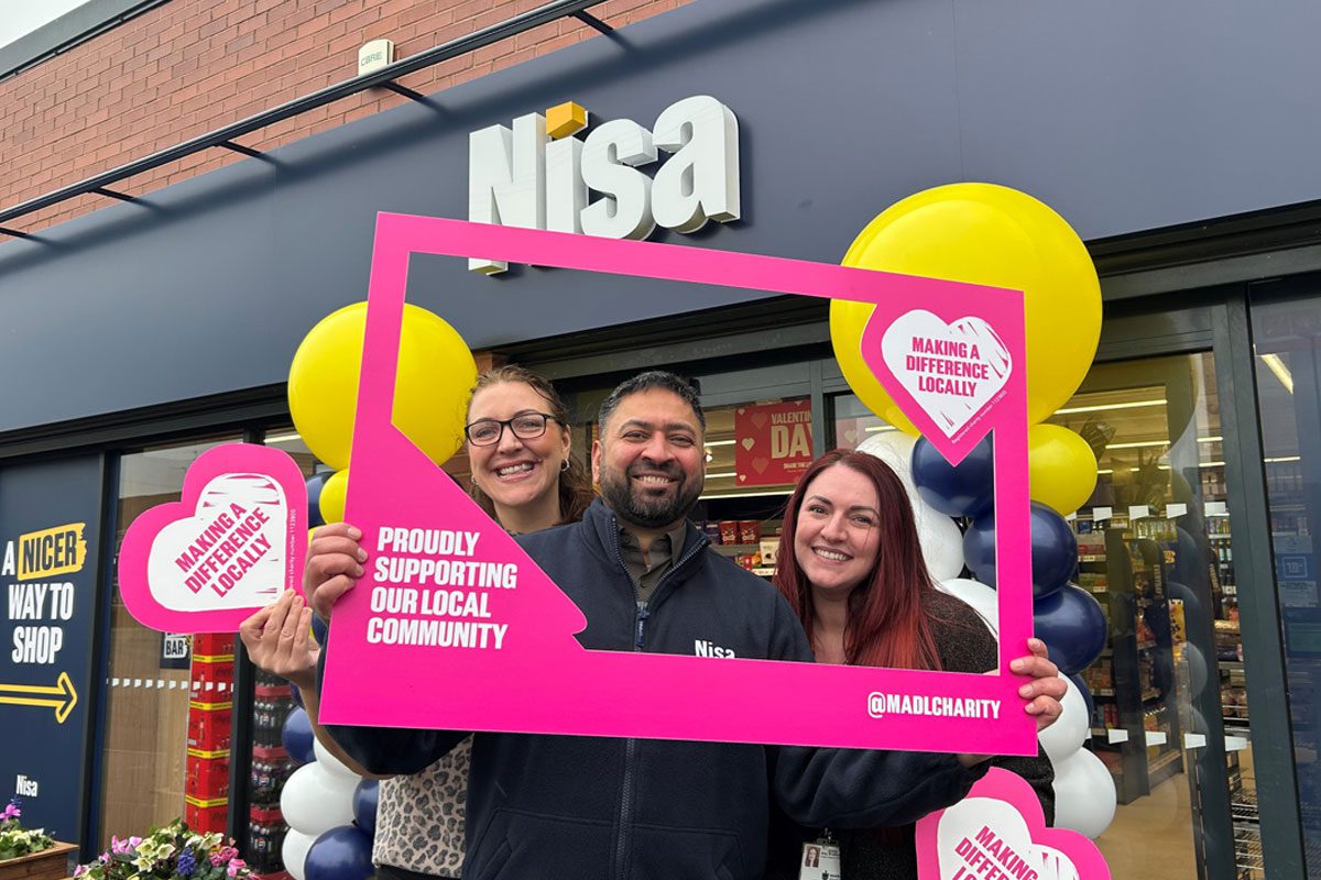 A group of people stand outside a Nisa store with a Making a Difference Locally banner around them.