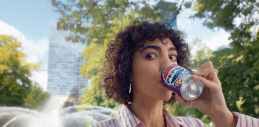 Pepsi launches summer campaign for ice cream flavours A woman sits drinking from a can of Pepsi Cherry & Vanilla Flavour in a park.