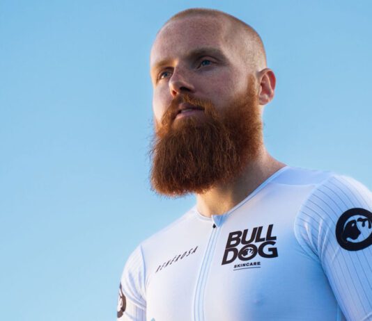 Bulldog marks sponsorship of IronMan with Russ Cook Endurance athlete Russ Cook stands against a blue background wearing a Bulldog Skincare branded top.