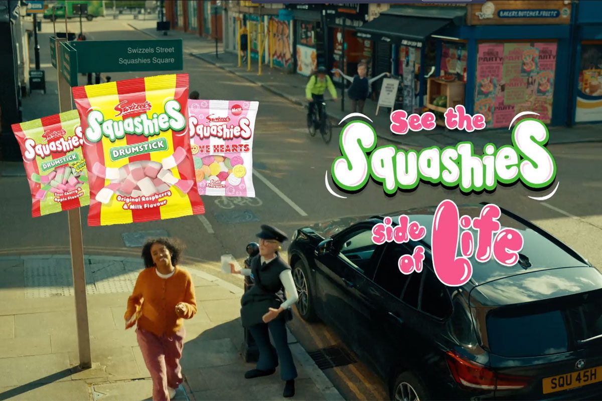 A still image from the 'See the Squashies side of life' ad campaign for Swizzels with a woman walking down a street with inflatable characters near her. Packs of Swizzels Squashies variants are also included in the imagery.