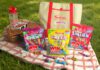 Swizzels launches Day Out With The Kids promo packs A picnic scene with variety packs of Swizzels sweets, a picnic blanket, a basket, sunglasses, a water bottle and an insulated bag with the Swizzels and Day Out With The Kids logo on the front of it.