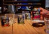 Wee Smoky taps into RTD demand with cocktail range A table with Wee Smoky cocktail cans on it and glasses with a person holding one of the cans in their hand.