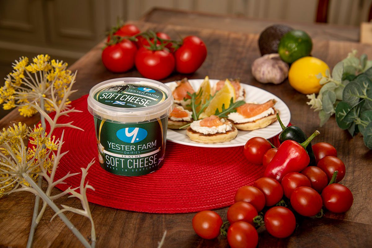 A tub of Yester Farm Dairies Soft Cheese sits next to a plate with canapés on it and different foods around the plate.